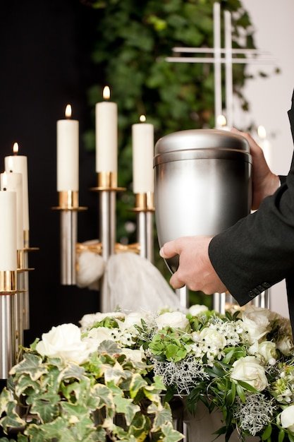 man-taking-funeral-urn-with-candles-flowers